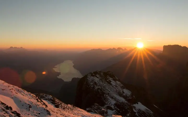 Pogled iz zraka na planinu obavijenu oblacima pod svjetlom zalazećeg sunca i plavim nebom.