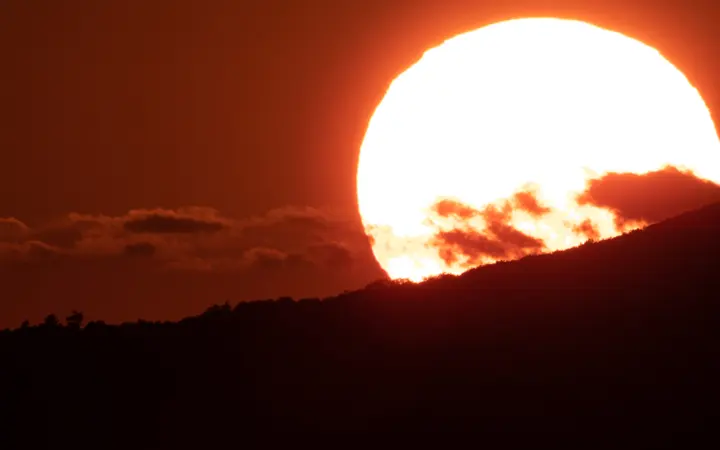 Planinski vrhovi u zlatnom sjaju zalaska sunca s prisutnim oblacima i prirodnim krajolikom.