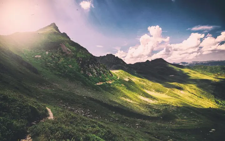 Zelene livade i brežuljci okruženi planinama pod oblacima stvaraju široki pejzaž.