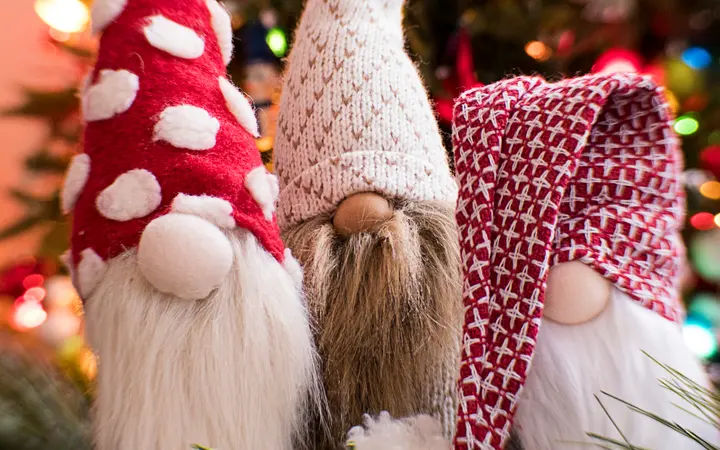 Patuljak s bradom i crvenom kapom na blagdanskoj pozadini s bokeh efektom i toplim tonovima.