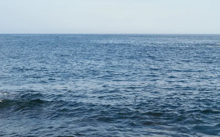 Svježi plavi val oceana na obali s vidljivim horizontom i čistim nebom u pozadini.