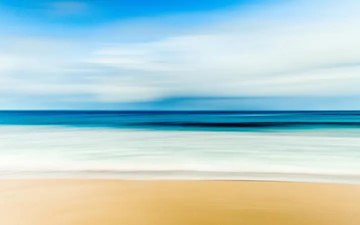 Mekana pješčana plaža s lagano zamagljenim horizontom i plavim morem u daljini pod dnevnim svjetlom.