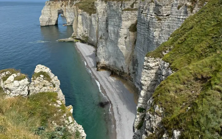 Pješčana plaža i litice uz obalu u uvali s plavim morem i prirodnim dnevnim svjetlom.