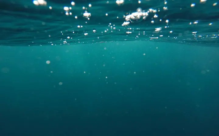 Plava voda s mjehurićima na površini u prirodnom okruženju oceana.