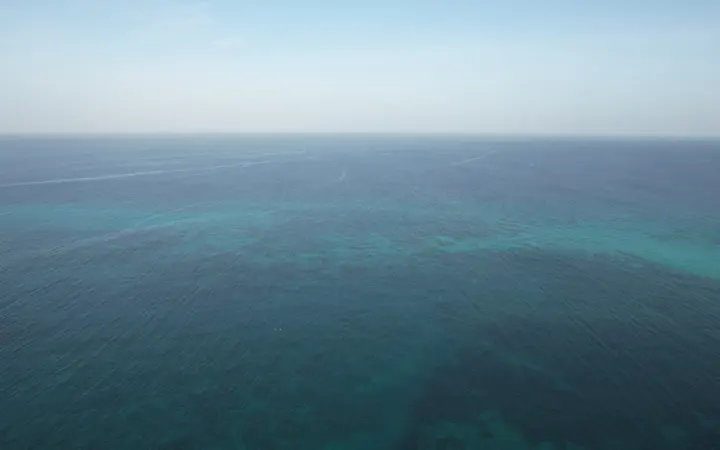 Mirna plava površina oceana snimljena iz zraka pod vedrim nebom bez oblaka.