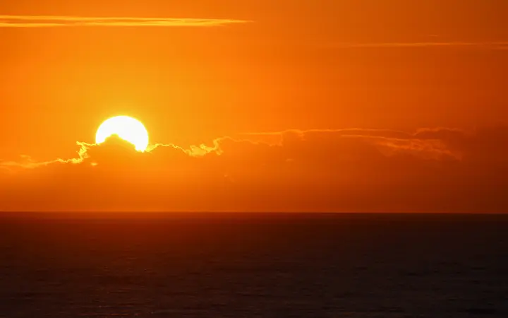 Topli zlatni tonovi obasjavaju oblakom obojeni horizont u mirnoj večernjoj atmosferi.
