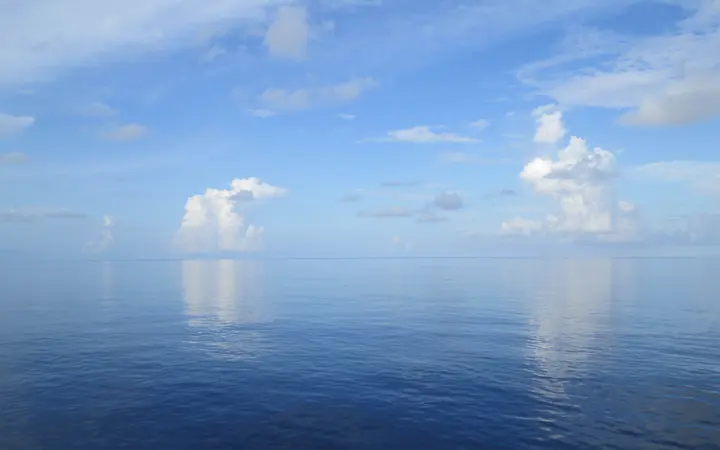 Vedro nebo s ponekim oblakom širi se iznad oceana u prirodnom krajoliku.
