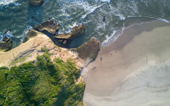 Pogled iz zraka na obalu s pješčanom plažom i plavim morem pod vedrim nebom.
