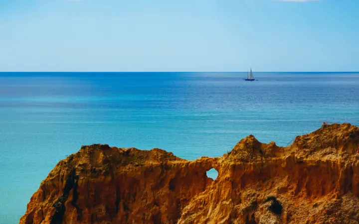 Plave stijene i ocean s brodom u uvali pod vedrim plavim nebom.