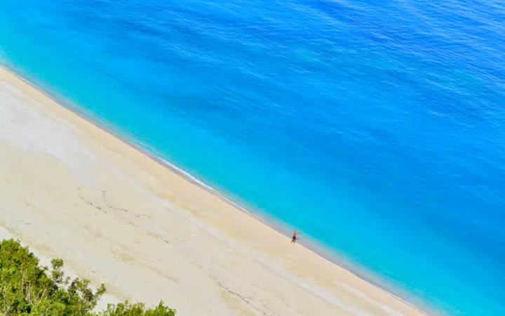 Jasno tirkizno more dodiruje pješčanu plažu uz obalu otoka Cephalonia.