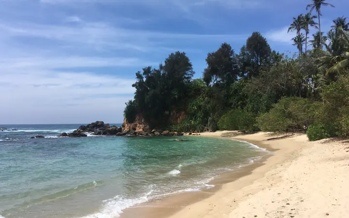 Pogled na pješčanu plažu i plavo more u uvali uz obalu pod vedrim nebom.