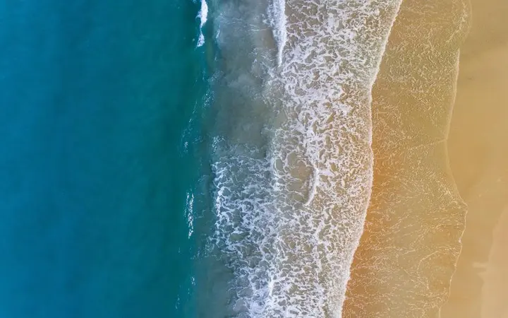 Pješčana plaža i plavo more pod vedrim nebom s pogledom iz zraka.