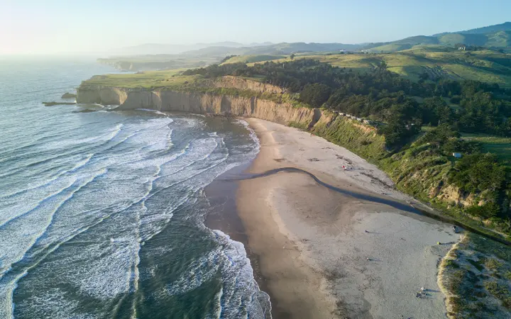 Zračni pogled na zelenu obalu s pješčanom plažom i stjenovitom liticom.