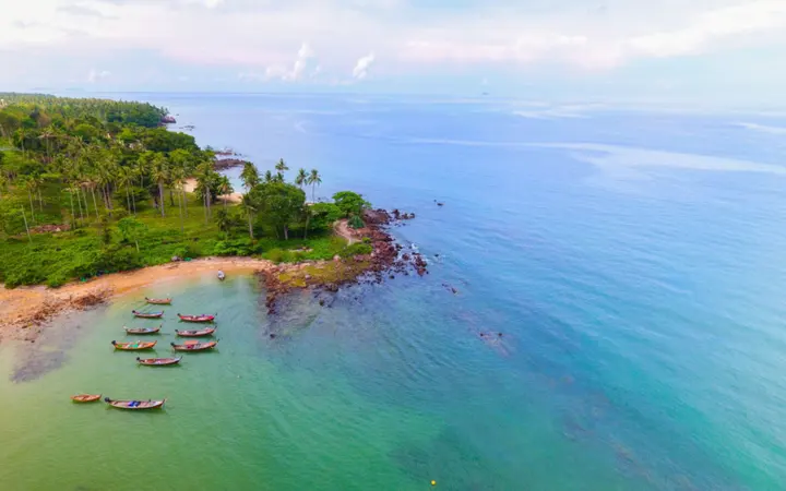 Pješčana plaža s kanuima i brodovima na obali u egzotičnom okruženju.