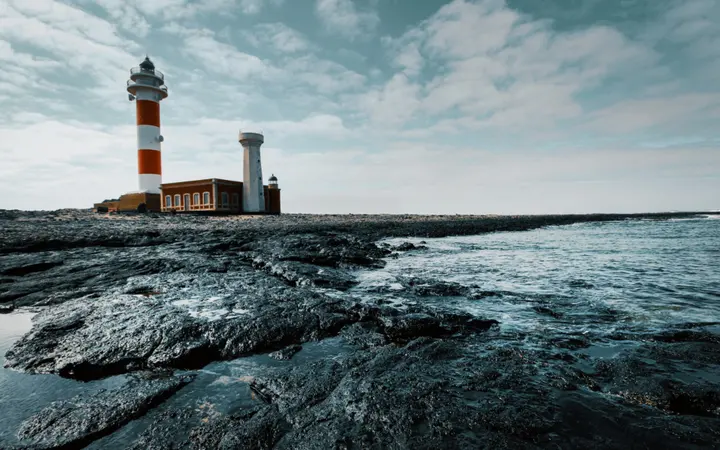 Bijeli svjetionik stoji na stijenama uz ocean pod dnevnim svjetlom.