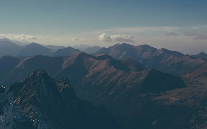 Visoke planine s oštrim liticama pod oblačnim nebom stvaraju dramatičan i pustolovni prizor.