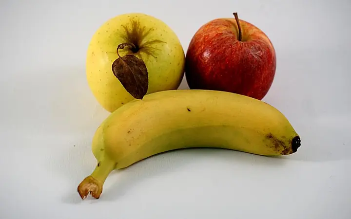 Svježe banane i jabuke s lišćem na pozadini u prirodnim bojama.