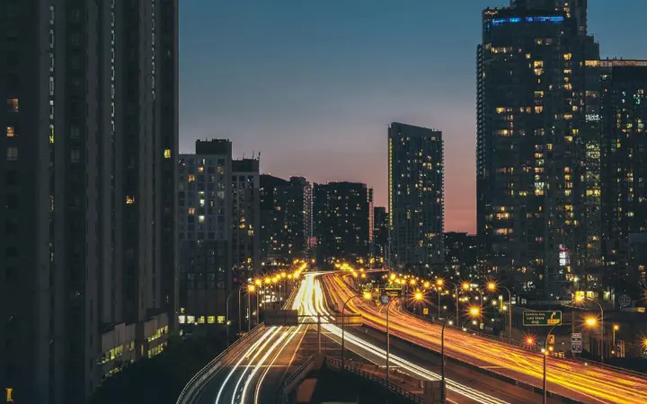 Pogled na gradsku panoramu s visokim zgradama i automobilima u sumrak s toplim bojama.