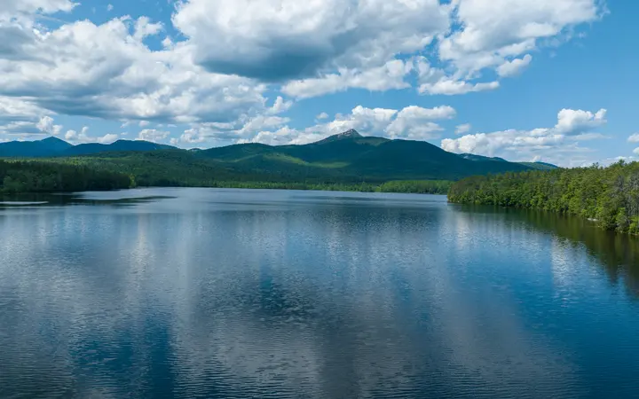 Plavo nebo s oblacima nad zelenom šumom i planinskim krajolikom u smirenoj atmosferi.