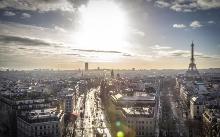 Zgrade pod plavim nebom s oblacima i svjetlom koje obasjava gradsku panoramu.