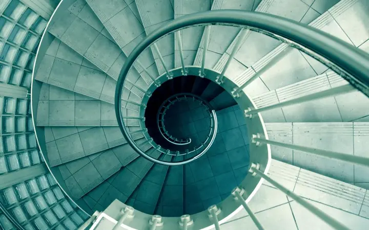 Uske spiralne stepenice s metalnom ogradom u modernom dizajnu s naglaskom na geometriju i svjetlost.