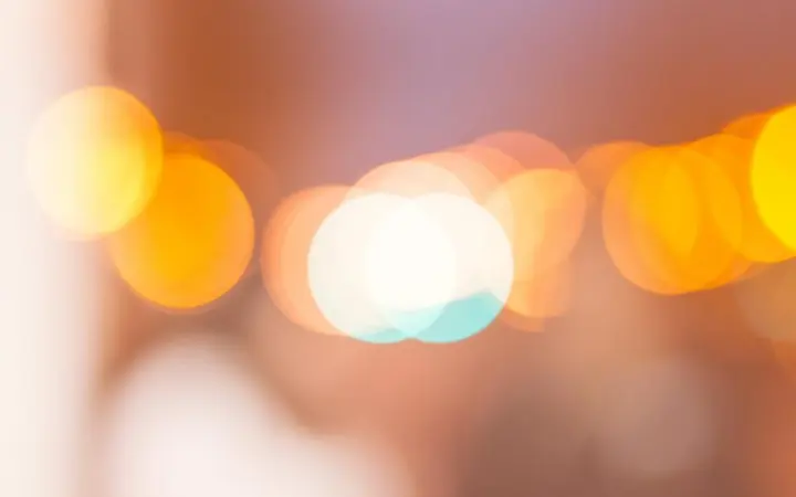 Svijetli žuti bokeh krugovi na tamnoj pozadini stvaraju topli i nježni svjetlosni efekt.