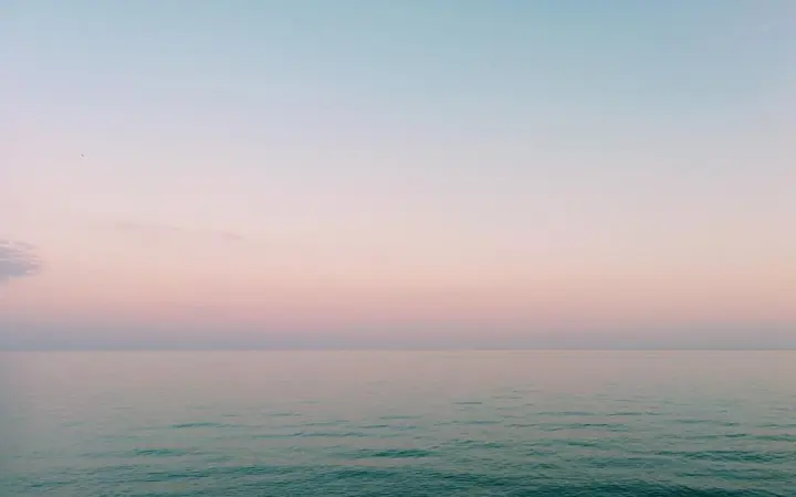 Smirena morska voda s nježnim prijelazima plave i ružičaste boje u pozadini.