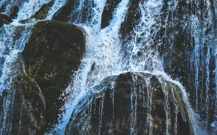 Vodopad okružen liticama i stijenama u području Jiuzhaigou s vidljivim prskanjem vode.