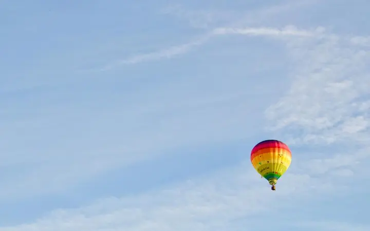 Šareni zračni balon lebdi na plavom nebu s vedrim bojama.