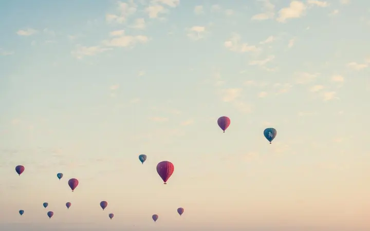 Zračni balon s košarom leti među oblacima u raznobojnom okruženju.