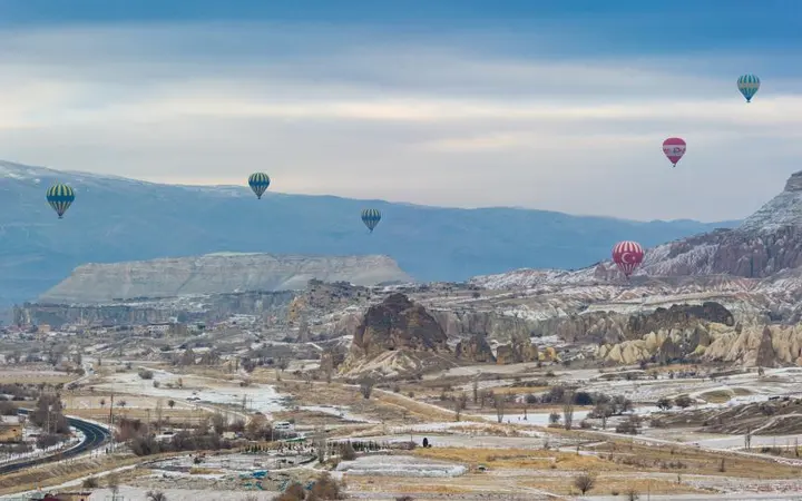 Zračni balon leti iznad planinske visoravni s oblacima u pozadini.