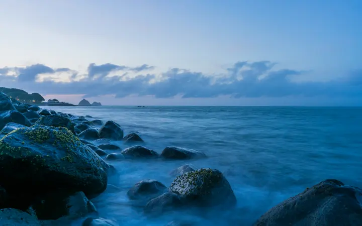 Prostrani plavi ocean ispod svijetlog neba s mekanim oblacima u pozadini.