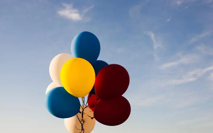 Veseli šareni zračni balon lebdi među mekanim oblacima na plavom nebu.