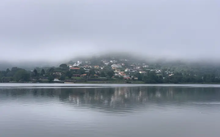 Mirno jezero okruženo jesenskim drvećem obavijeno je gustim slojem magle u zoru.