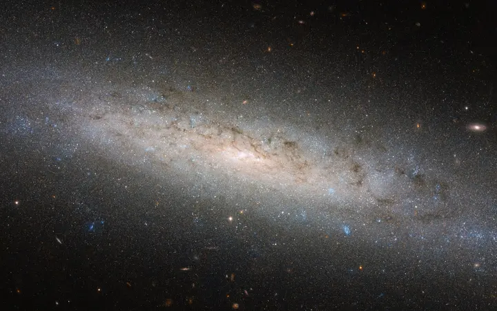 Disk spiralne galaksije NGC 24 sjaji u tamnim plavim nijansama na crnoj pozadini.