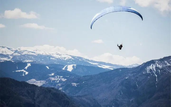 Snimka snježnih planina s paraglajderom u letu pod plavim nebom i širokim pogledom.