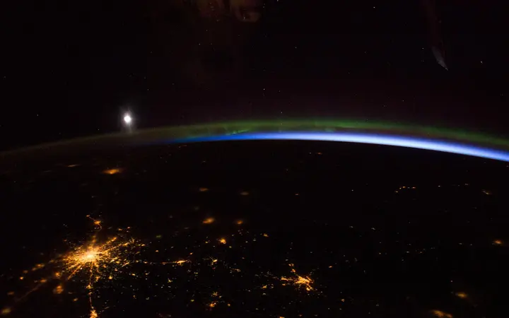 Noćna scena s aurorom borealis i Mjesecom iznad Moskve u hladnim plavim i zelenim tonovima snimljena iz svemira.