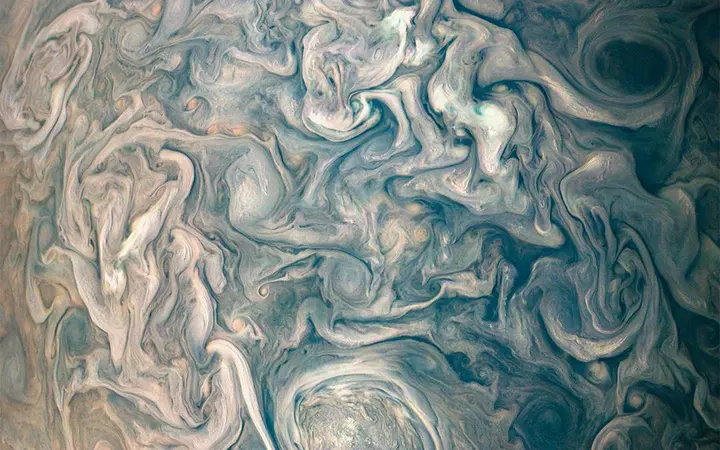 Vrtložni i nemirni oblačni pojasevi sjeverne hemisfere Jupitera u živim bojama i dinamičnim oblicima.