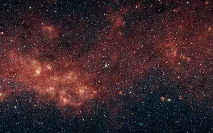 Zvijezde galaksije skrivene su iza gustih oblaka prašine, prikazane u toplim infracrvenim tonovima.