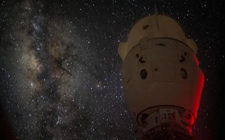 Galaksija se pojavljuje u pozadini iza slabije osvijetljenog svemirskog broda Dragon Endeavour.