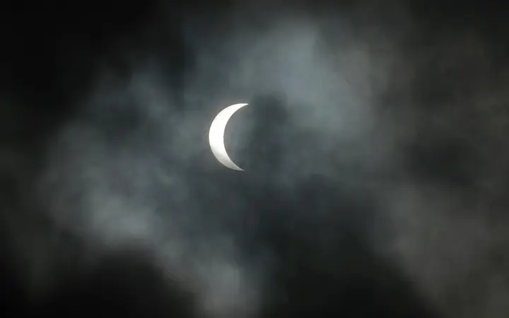 Mjesec djelomično prekriva Sunce pod oblačnim nebom u New Orleansu, uz 85% pomrčine u sivim i žućkastim tonovima.