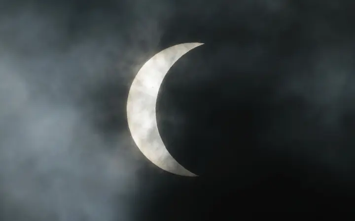 Mjesec polako zaklanja Sunce pod pretežno oblačnim nebom u New Orleansu s vidljivom sjenom pomrčine.